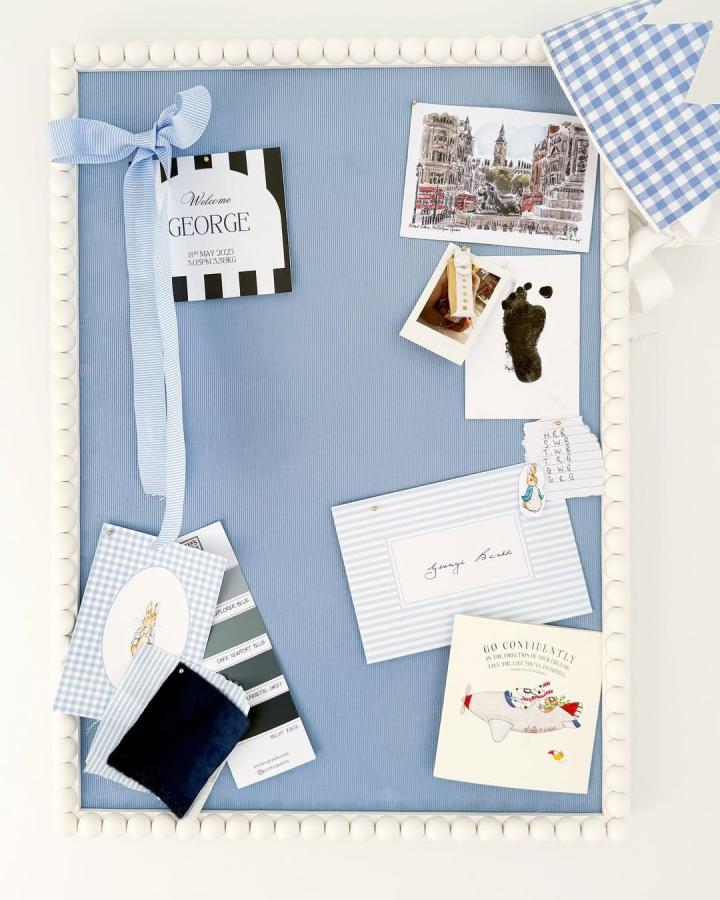 Blue fabric-covered cork board with white pin trim and gingham accents from @harrietlanestudio beautifully styled with cards and keepsakes.