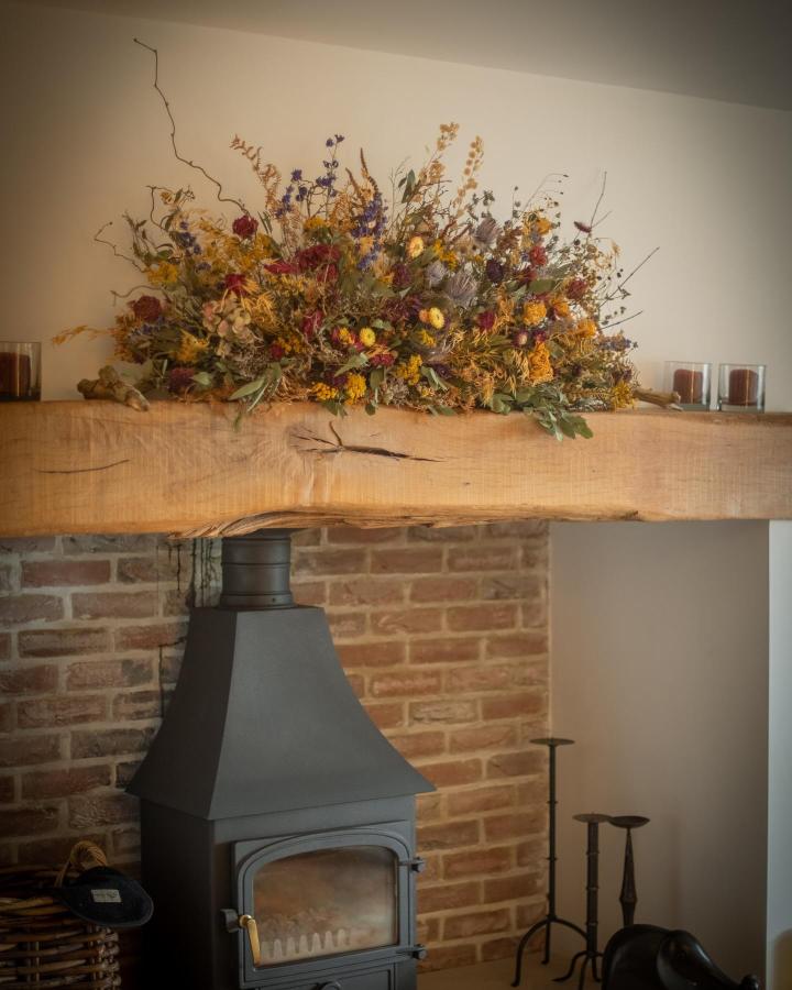 Vibrant mixed dried floral mantelpiece display from @brackenandfleur featuring warm autumn hues and natural textures above a wood stove.