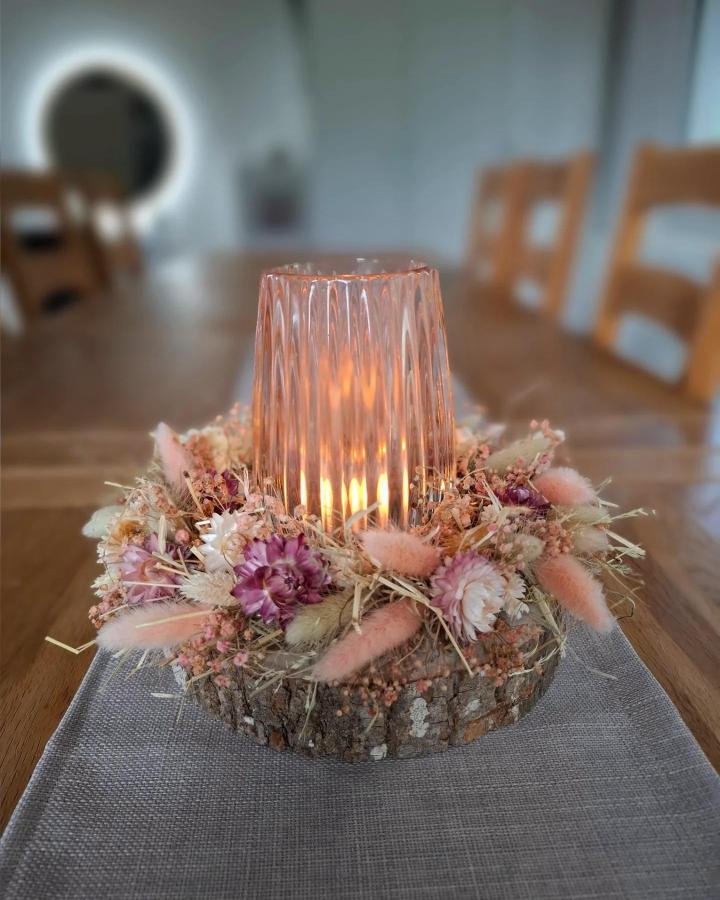 Pink and lavender dried flower centerpiece with rustic wood base and glass candle holder from @haarstubae on wooden table. Cozy and natural vibe.