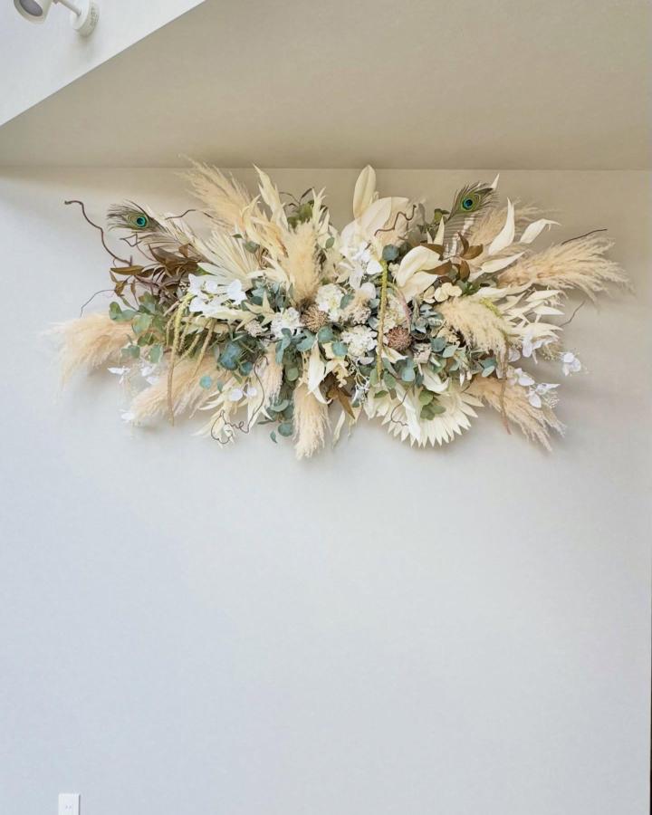 Neutral and natural toned dried floral wall decor from @popot_rico with pampas grass, eucalyptus, and peacock feathers creating texture and depth.