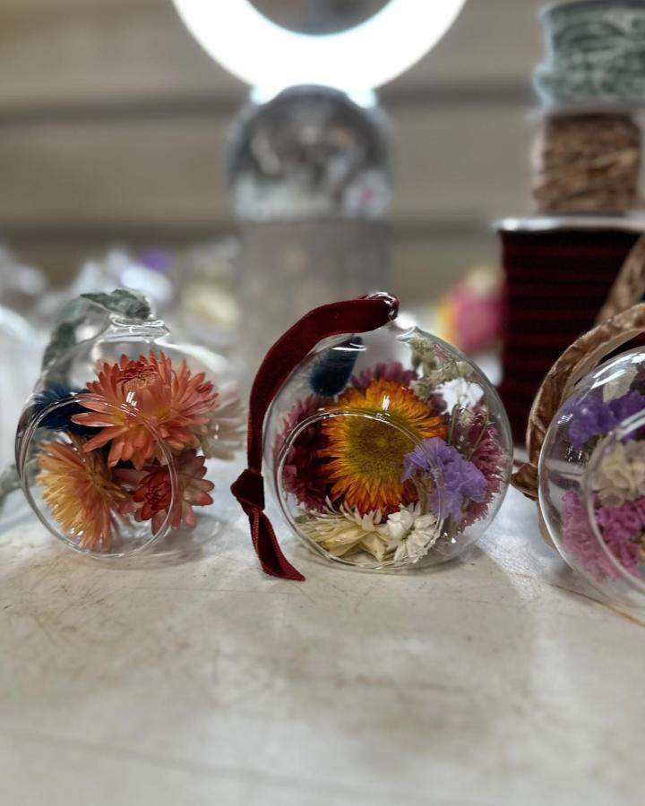 Clear glass globe ornaments filled with peach, yellow, and lavender dried flowers from @thewildfireweed showcasing dried flower crafts. Bright yet soft arrangement.