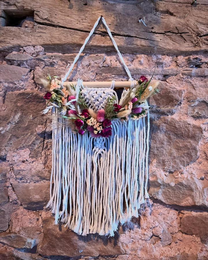 Macrame wall hanging with burgundy and peach dried flowers on rustic stone wall by @fromeparkposies. Textured and boho style decor.