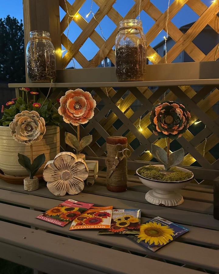 Layered peach cream fabric flowers with moss base and wooden sticks on outdoor patio by @knotperfectdesignsco. Crafty floral décor with rustic charm.