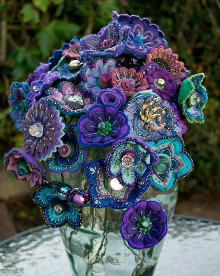 Purple and teal felt flower bouquet with bead and button accents by @doableyou in a glass vase outdoors. Vibrant handmade blooms.