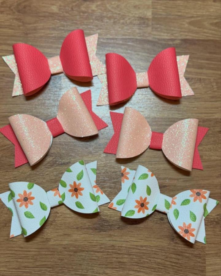 Red and peach textured layered bows with floral print on wood surface by @pas_de_deux_designs. Handmade faux leather accessories.