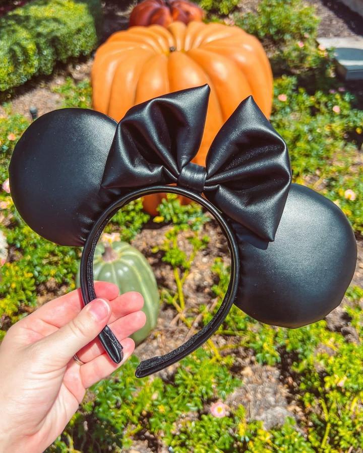 Black faux leather Minnie ears headband with a large bow, held in hand outdoors by @parkhopperdesign showing smooth shiny texture.