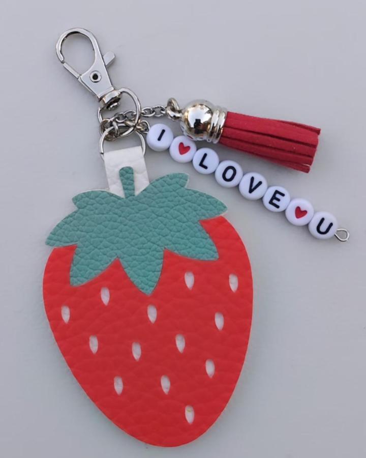 Red and green textured faux leather strawberry keychain with red tassel and love bead charm from @canicavanlog. Cute accessory detail.