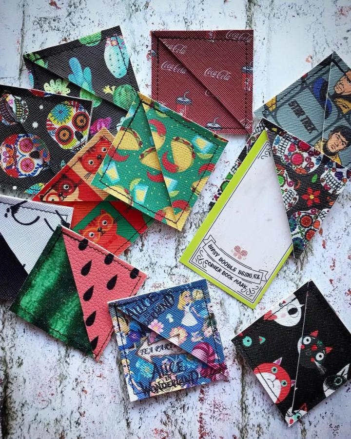 Bright patterned faux leather corner bookmarks laid out on a rustic white wooden surface from @dipsydoodledesignz. Various quirky and colorful prints create a cheerful reading accessory display.