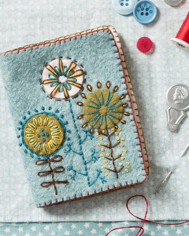 Dusty blue felt needle book with mustard and cream floral embroidery from @stitchedmodern featuring cozy handmade stitching.