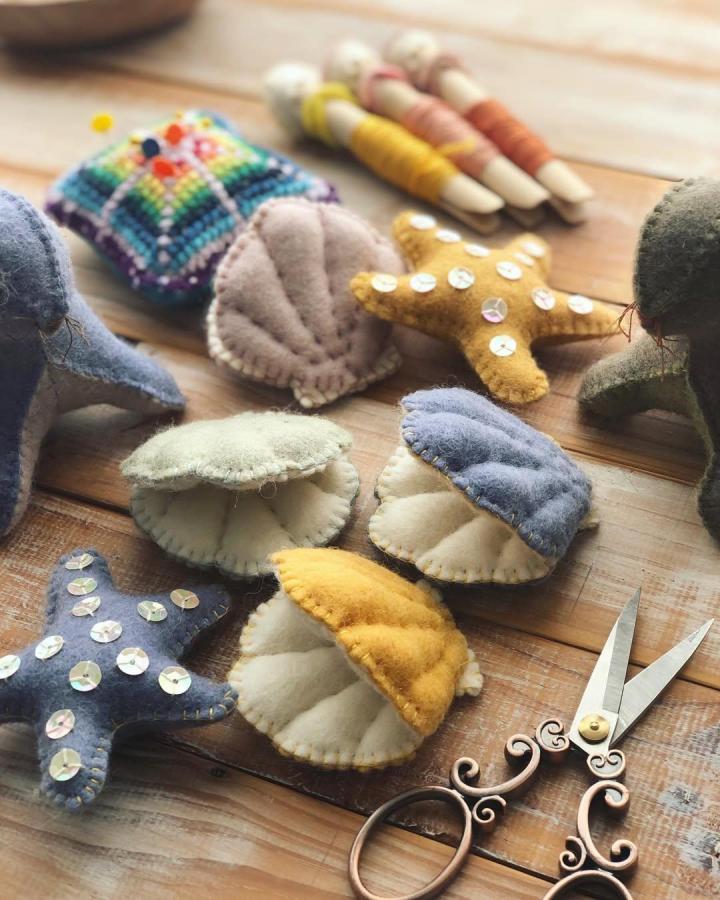 Yellow and pastel felt seashells and starfish crafts on wooden table by @yuki_australia. Handmade, cozy seaside-inspired decor with sequins and stitching.