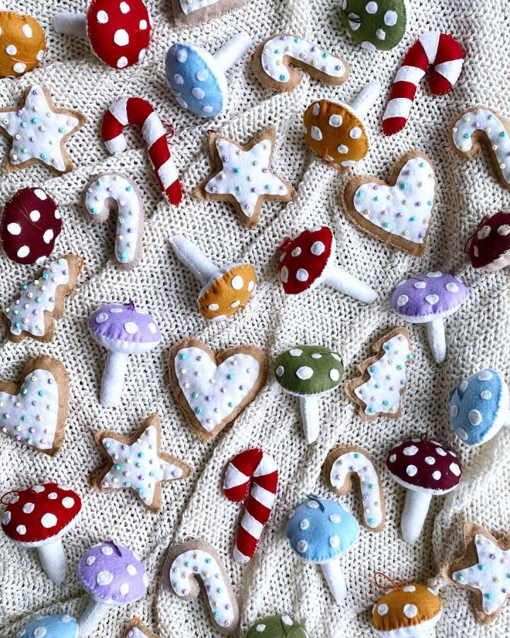 Red, mustard, purple, and blue felt mushrooms and candy cane ornaments on knitted cream background from @shop.granolafairy with soft white dot details and pastel beads.