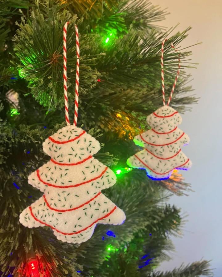 White felt Christmas tree ornaments with green stitch details and red thread from @kellisfeltkitchen. Hand-sewn holiday decorations hanging on tree branches.