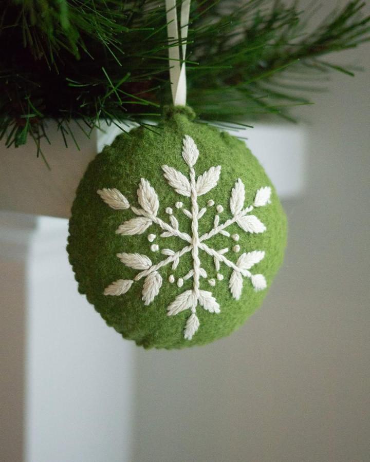 Green felt ornament with cream embroidered snowflake hanging on tree by @little.oak.design.co showing felt ornament ideas in a cozy setting.