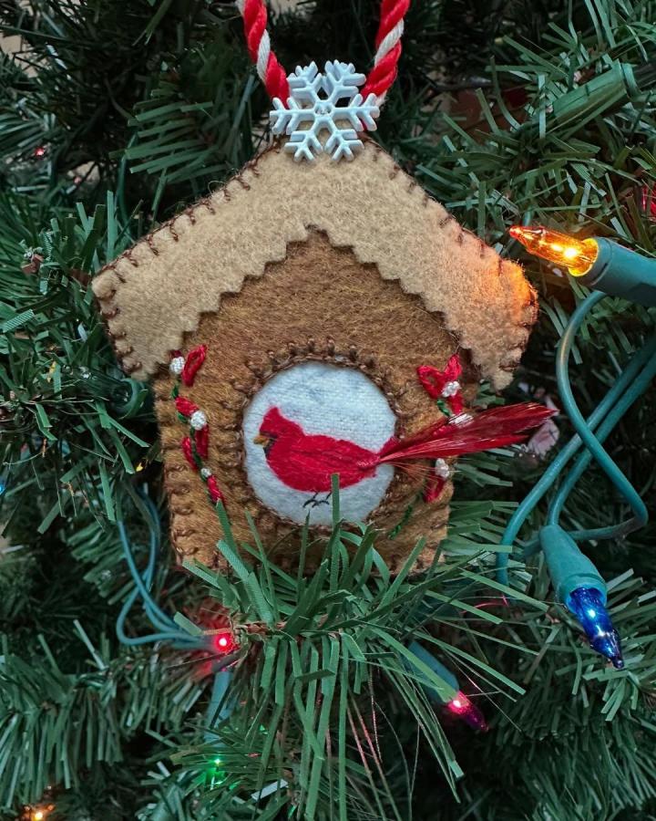 Brown and tan felt birdhouse ornament with red cardinal and embroidered details on Christmas tree from @anastasia_in_wonderland. Hand-stitched cozy winter decor.