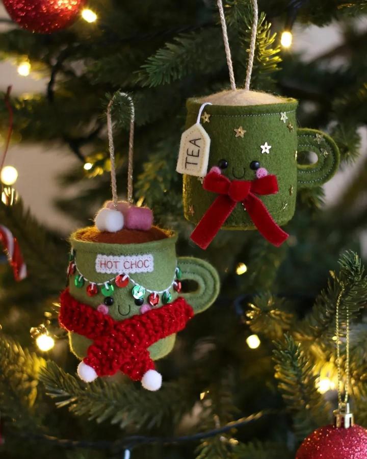 Green felt cup ornaments with scarves, bows, sequins, and pom-poms by @hannahdoodlecrafts showing felt ornament ideas. Cozy and detailed holiday crafts.