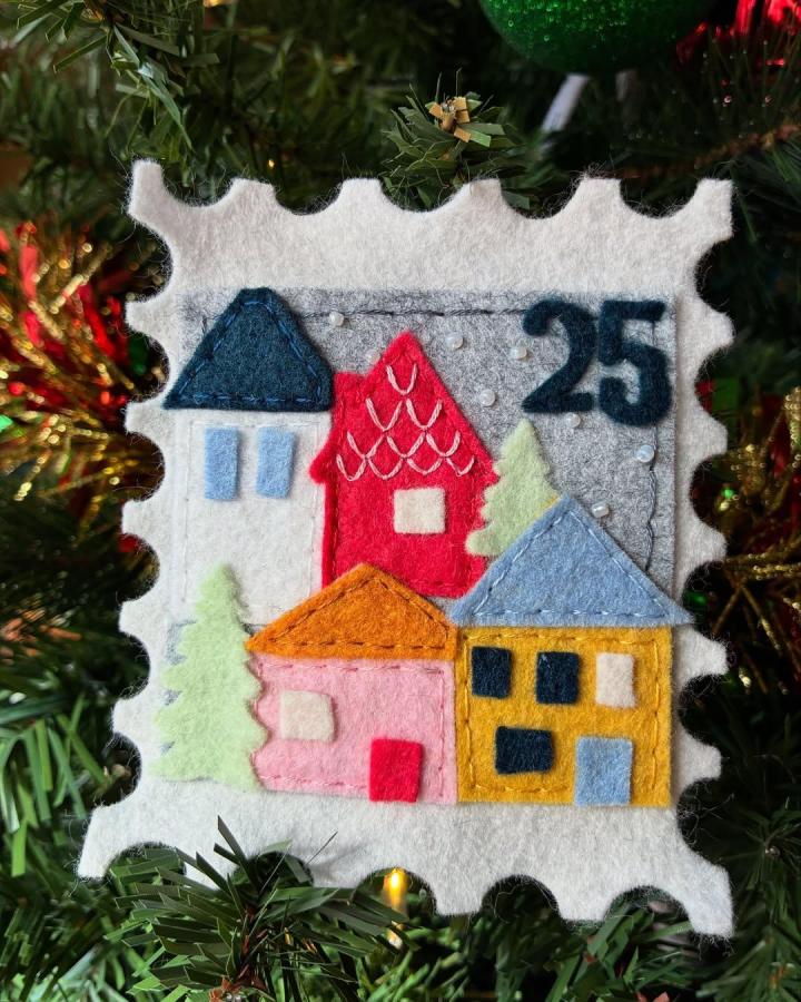 Colorful felt village ornament on tree from @foureyesfibers featuring layered homes with stitched details and a snowy winter theme.