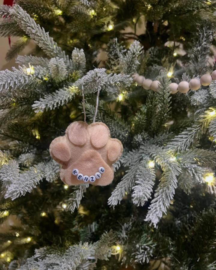 Light brown felt paw ornament with personalized name beads on a frosted Christmas tree from @thelittlefeltsprout featuring felt ornament ideas.