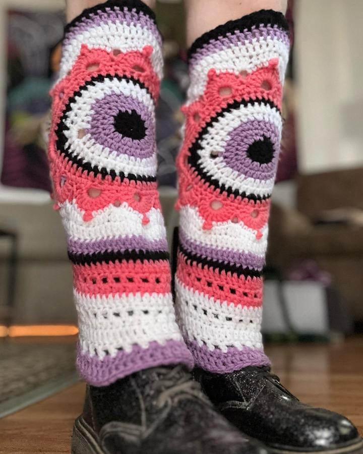 Pastel purple coral and white crochet leg warmers with eye motif and scalloped edges from @eclectic.wonderland. Bold, textured handmade accessory.