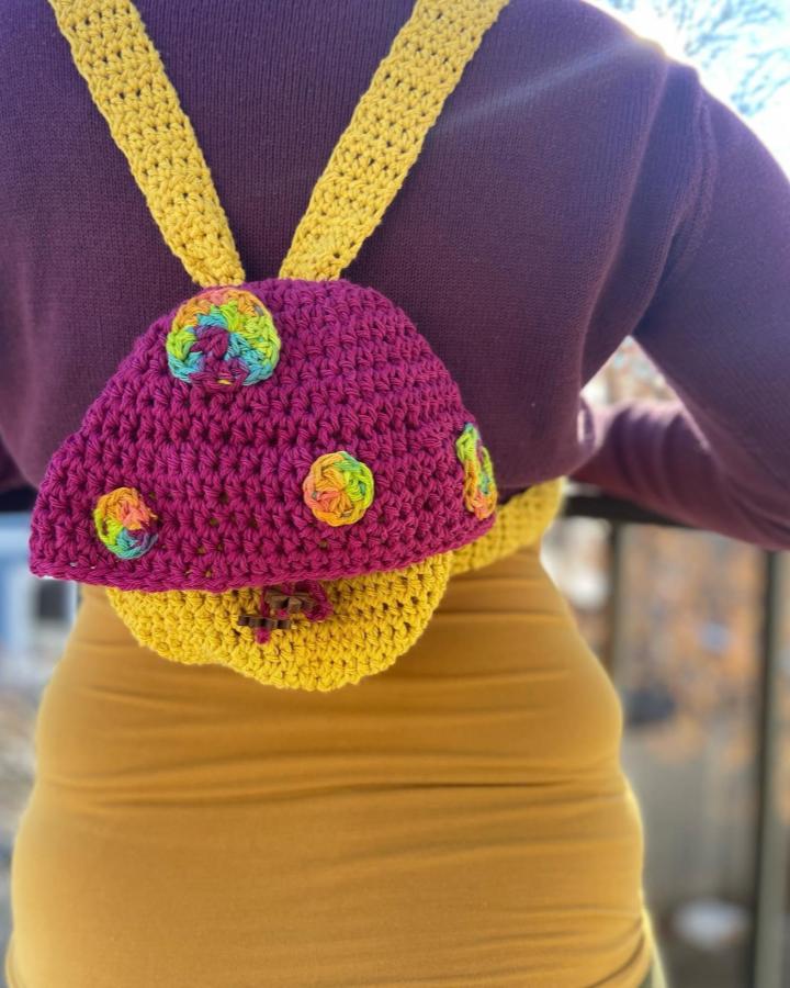 Bright raspberry and mustard yellow crochet mushroom backpack with colorful spots from @theweavingwook. Playful and bold handmade accessory.