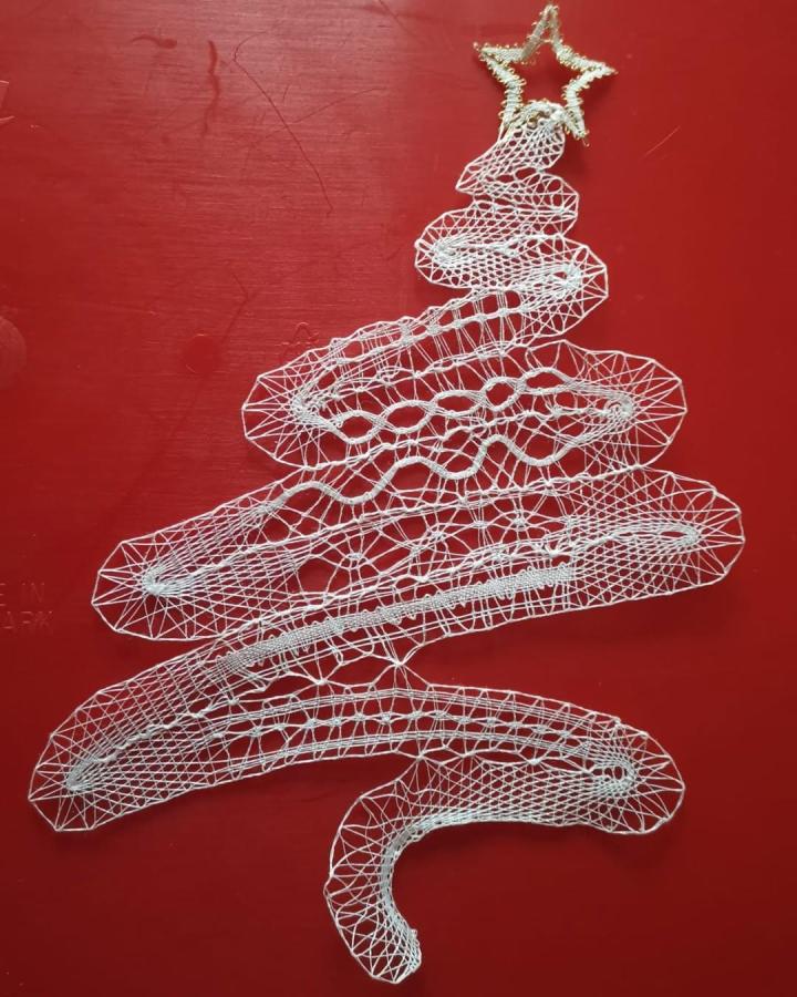 White delicate handmade lace Christmas tree wall art from @creatieveomaelly, intricately crafted with fine threads on a vibrant red background.