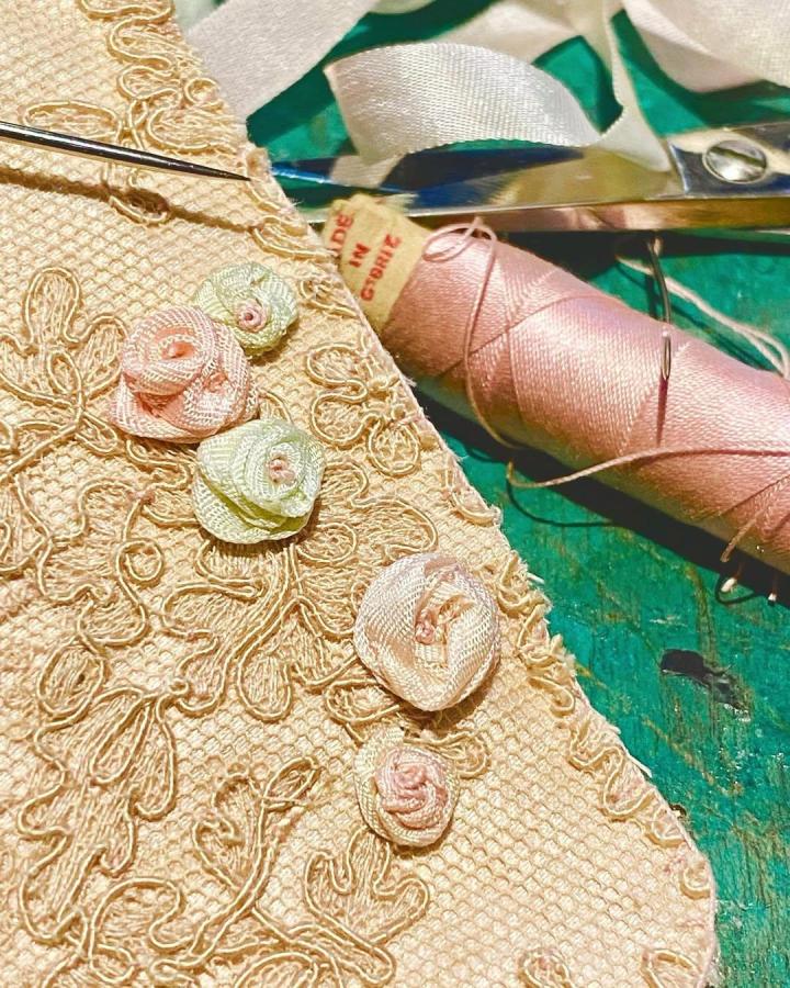 Vintage lace ribbon embroidery with pastel pink and green roses crafted by @little_burrow_designs close-up of delicate floral stitching and thread spool.