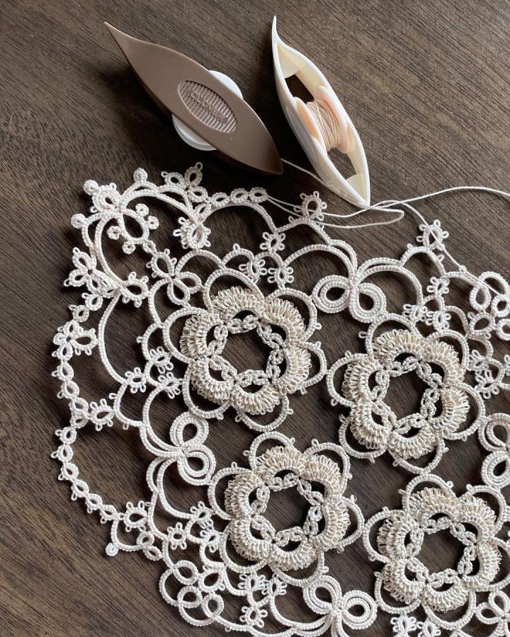 Cream-colored handmade tatted lace doily with floral patterns and tatting shuttles from @forgetmeknotto perfect for lace crafts for adults. Intricate and delicate design.
