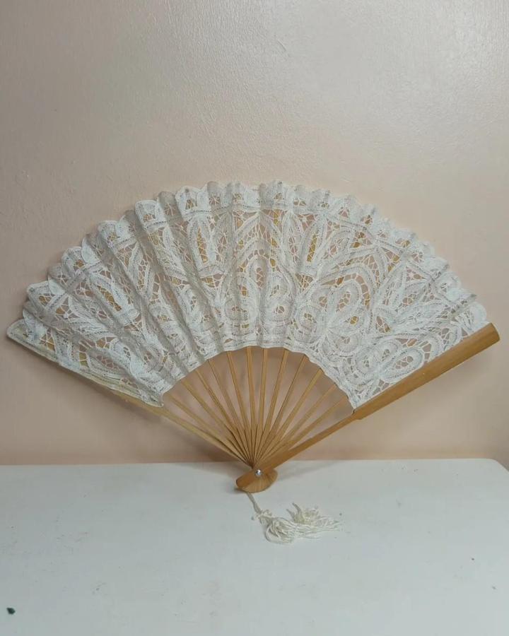 White lace fan with wooden ribs from @t.store.kenya. Elegant handmade piece with delicate swirling patterns and tassel detail.