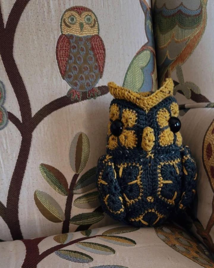 Crocheted navy and mustard owl with bead eyes on embroidered fabric from @zachtstout showing detailed yarn art and cozy handmade style.