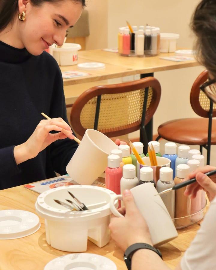 White ceramic mugs with pastel paint bottles and brushes from @bonbonpotterylondon showing detailed hand-painting art craft session.