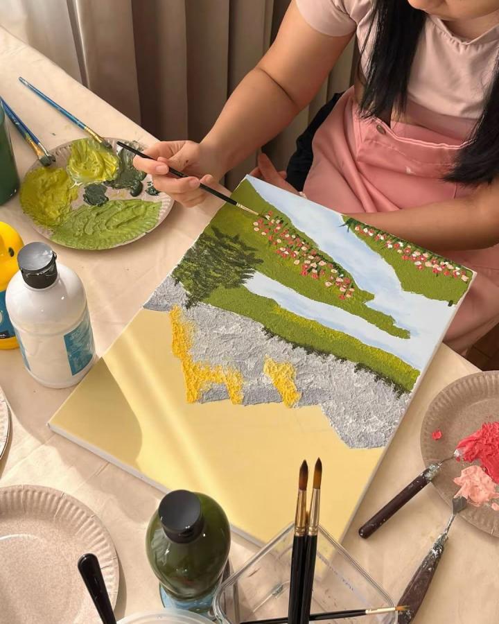 Textured landscape painting with green grass, pale blue river, and pink flowers by @bydolces showing tactile acrylic work.