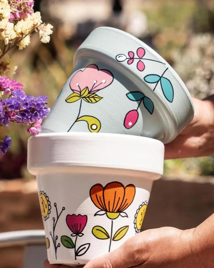 Brightly painted flower pots with whimsical floral designs in pastel and vivid colors from @rrdecohogar. Cheerful handmade garden craft.