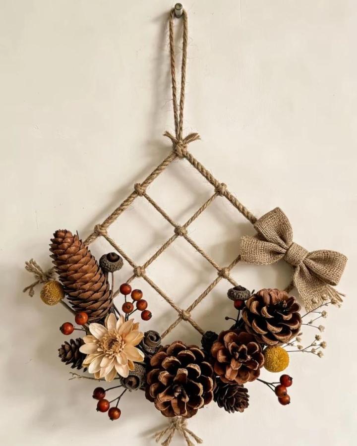 Natural pine cone wreath with burlap bow and twine frame from @the.artofpaper. Rustic hanging décor with berries and dried flowers.