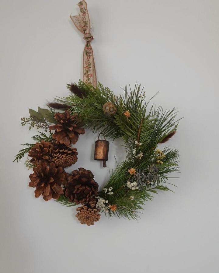 Brown pine cone and green pine needle wreath hanging on floral ribbon from @_withmiya. Natural rustic pine cone crafts for adults with floral and metal accent detail.