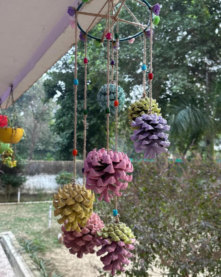 Pastel painted pine cones hanging with colorful beads from @explore_with_vingo. Outdoor wind chime craft with natural textures and bright accents.
