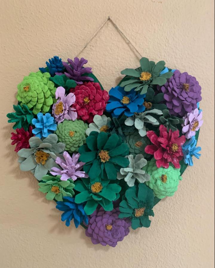 Brightly painted pine cone crafts for adults from @rosequeen56. Heart-shaped colorful flower wreath wall hanging. Vibrant and textured.