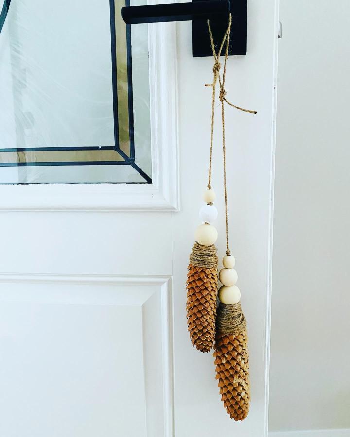 Natural brown pine cone tassels decorated with white wooden beads hanging from a black door handle by @vrenisplace. Simple rustic indoor decoration.