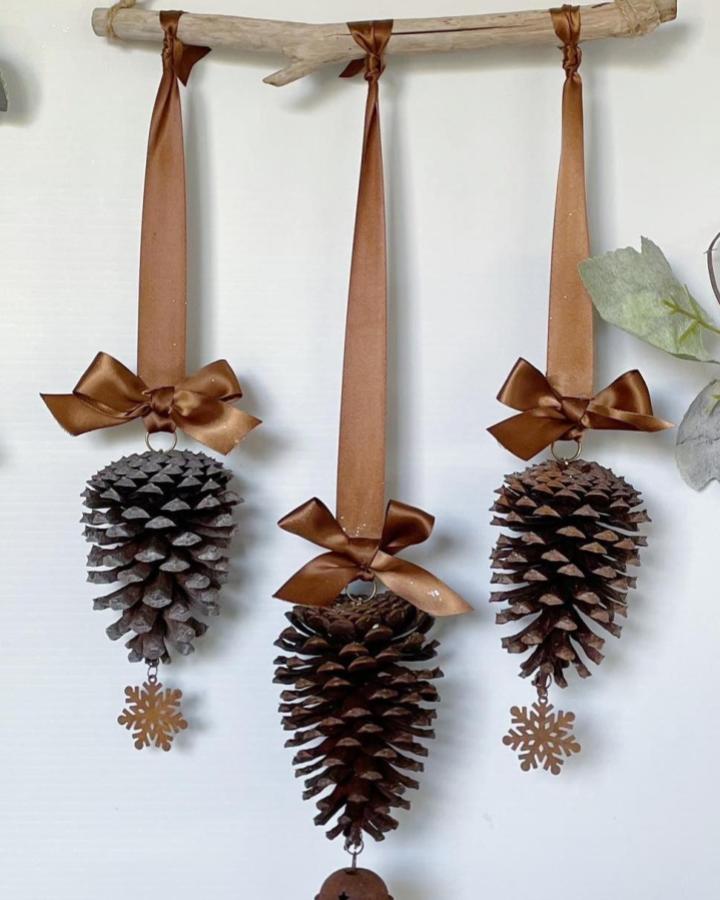 Bronze satin ribbon pine cone hanging ornaments with snowflake charms by @hangingaroundmacrame. Rustic winter decor with natural wood branch.