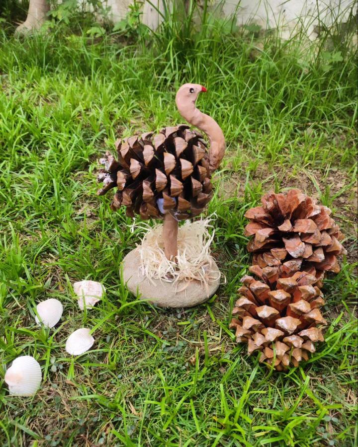 Pine cone flamingo craft with clay neck and raffia base from @i.think.art. Unique pine cone crafts for adults with natural and handmade details.