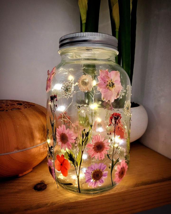 Pressed flower art ideas glowing fairy jar with pink and purple blooms and fairy lights from @creative.sparks.studio creating a warm decorative glow.