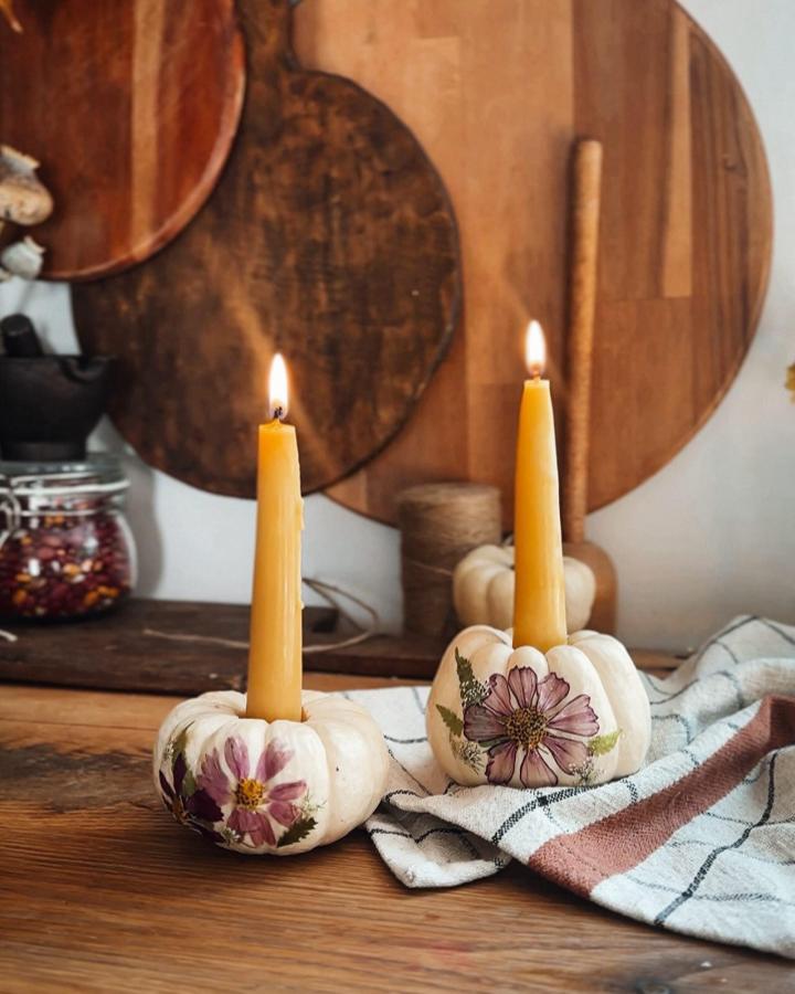 White mini pumpkins decorated with pressed pink flowers holding beeswax candles on a wooden table by @northwoodsfolk. Rustic fall décor with a floral touch.