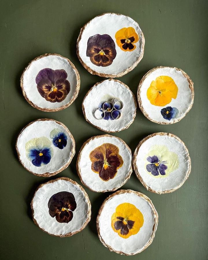 Pressed pansy trinket dishes on white clay with gold edges from @botaniquepress showcasing pressed flower art ideas. Bright and delicate.