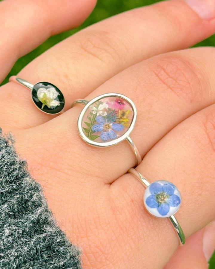 Blue and pink miniature floral rings from @castandclover. Silver bands highlight tiny preserved flowers in resin for unique jewelry.