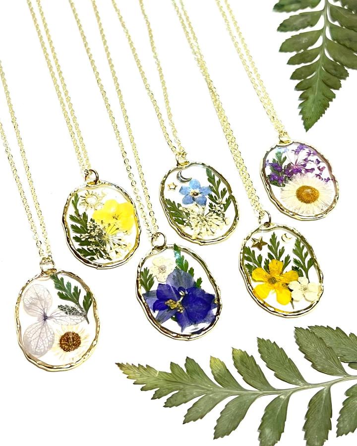 Yellow and blue pressed flower resin pendants with gold trim and fern accents from @wanderlustwares. Nature-inspired wearable art.