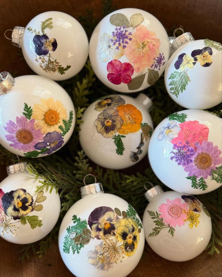 Pressed flower art ideas with vibrant pansy and daisy ornaments from @cloverhouse_vintage featuring delicate natural floral designs on white baubles.