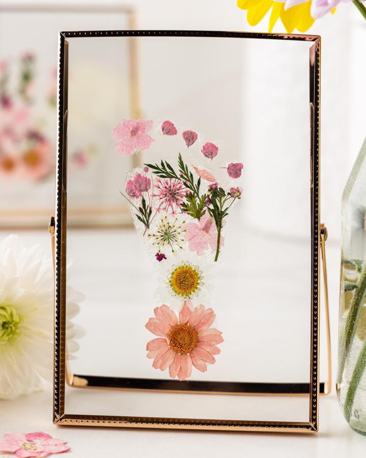 Pink and green pressed floral footprint in glass frame from @bestideasforkids. Delicate daisy and leaf arrangement with light shining through.