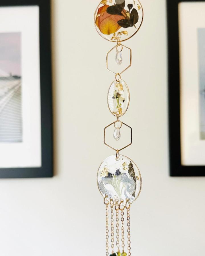 Amber and black floral resin sun catcher with gold accents and chains from @alwaysjean.jewels. Delicate, hanging botanical craft art.