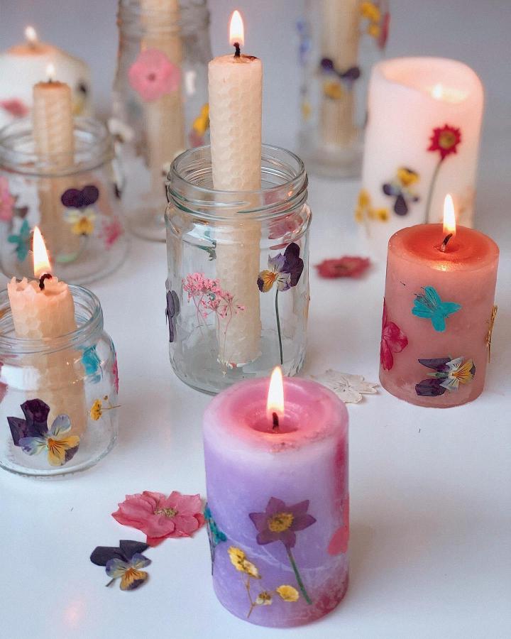 Glass jars and colored wax candles decorated with pressed wildflowers from @_dimity_ creating charming botanical candle holders.