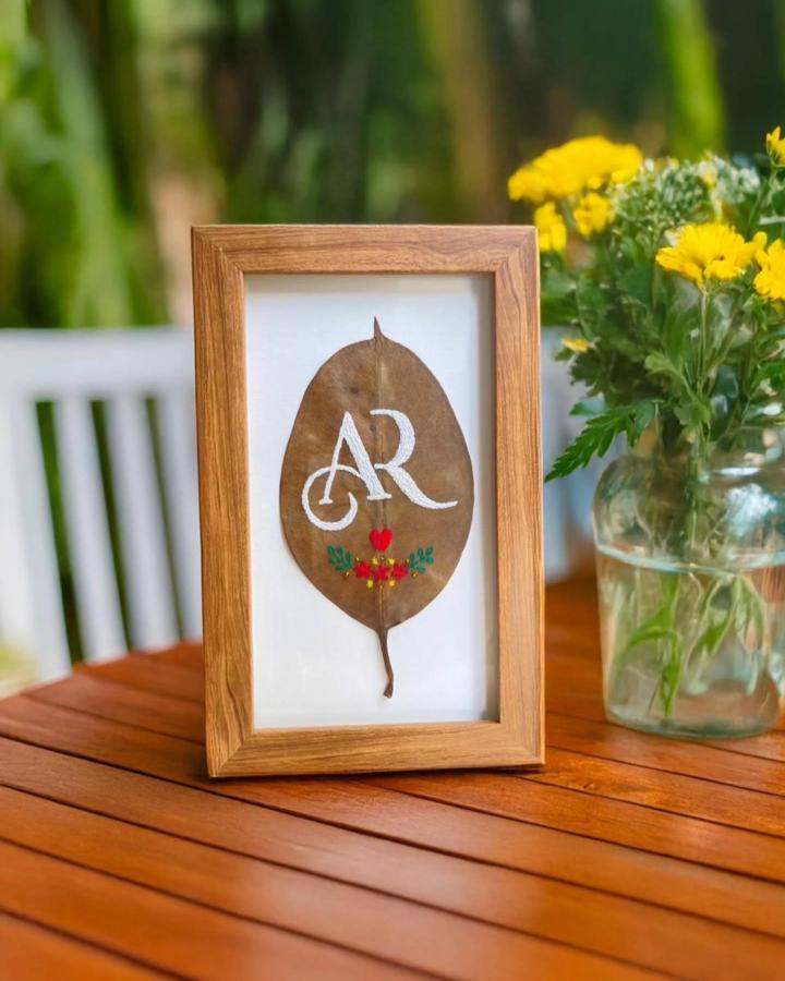 Pressed leaf crafts featuring a brown embroidered leaf framed as personalized nature art by @priyar_creation on a wooden table.