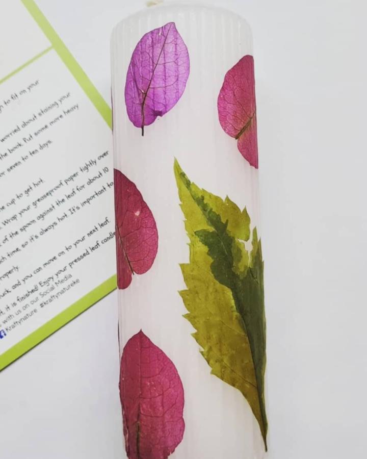 Pink and yellow pressed leaves decorate a tall white candle from @kraftynature showcasing delicate natural details.