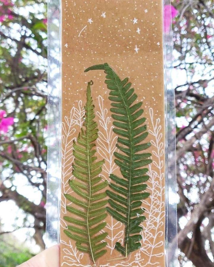 Pressed green fern leaf art on kraft paper with white ink doodles from @shilpajdesigns. Nature-inspired decorative craft piece.